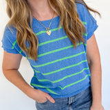 Woman wearing a blue and green striped shirt with jeans against a white wall.