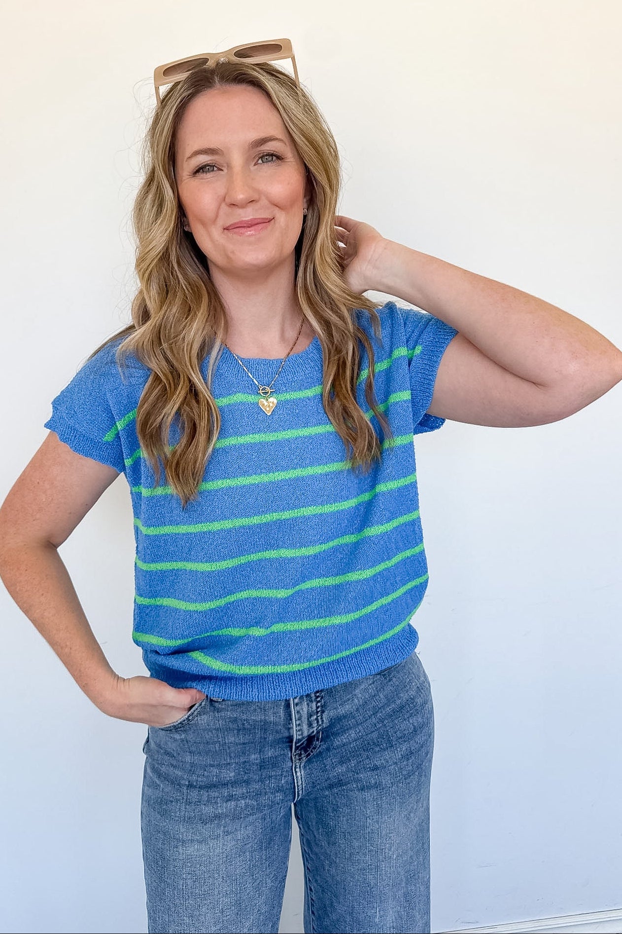 Woman wearing a blue and green striped shirt with sunglasses on her head against a white background