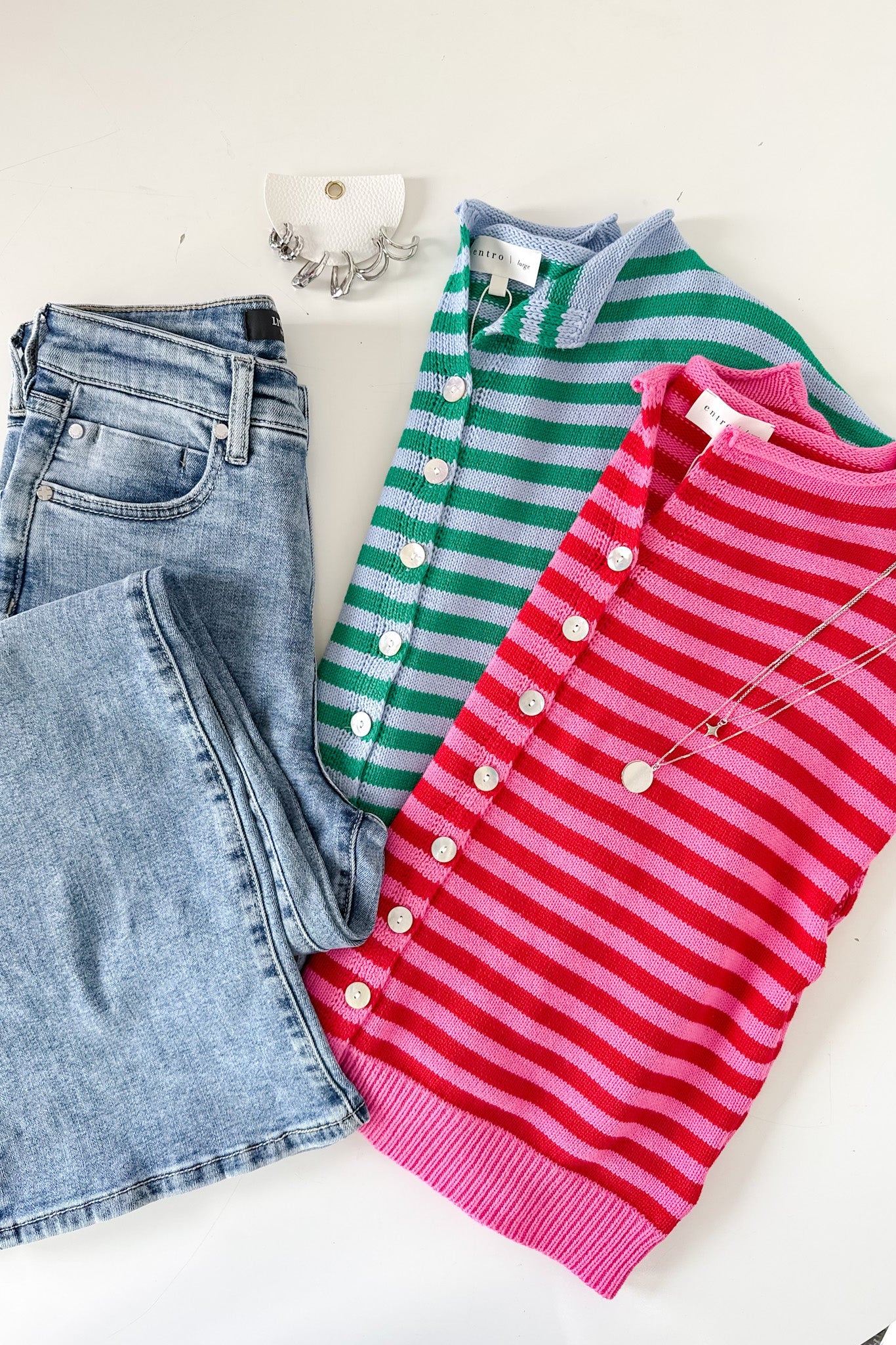 Two striped sweaters, one green and one pink, with a pair of blue jeans on a white surface.