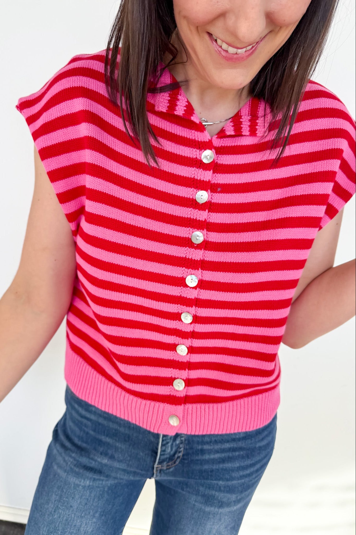 Person wearing a red and pink striped sleeveless cardigan against a white background