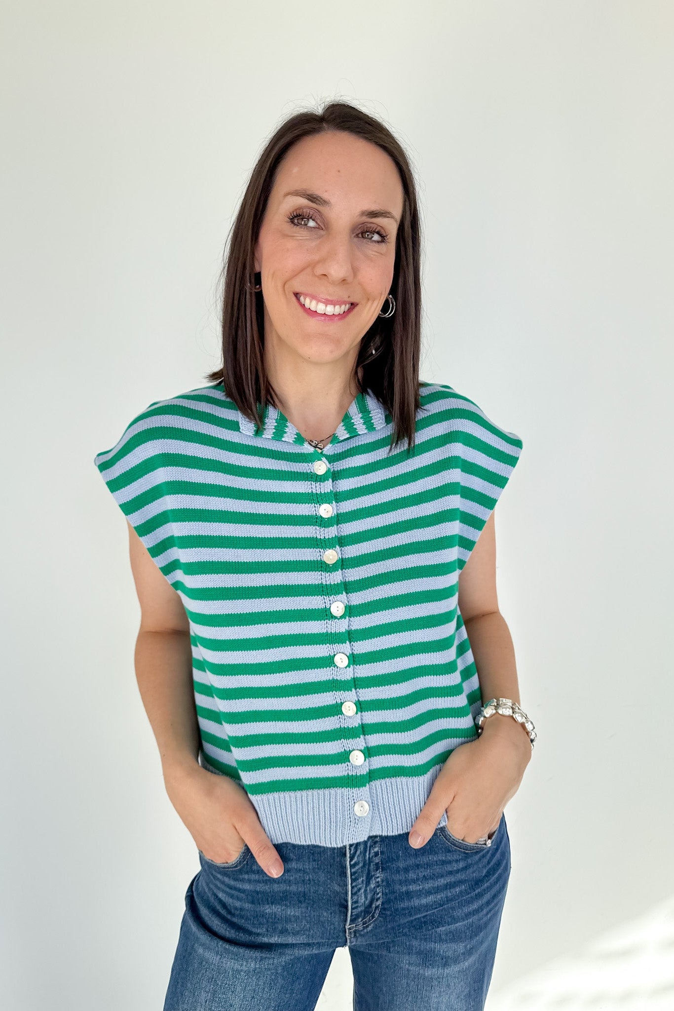 Woman wearing a green and white striped sleeveless cardigan against a plain background