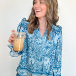Woman wearing a blue patterned blouse holding a glass of iced coffee against a white background