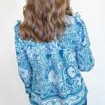 Person wearing a blue patterned blouse against a white background