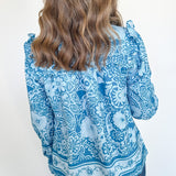 Person wearing a blue patterned blouse against a white background