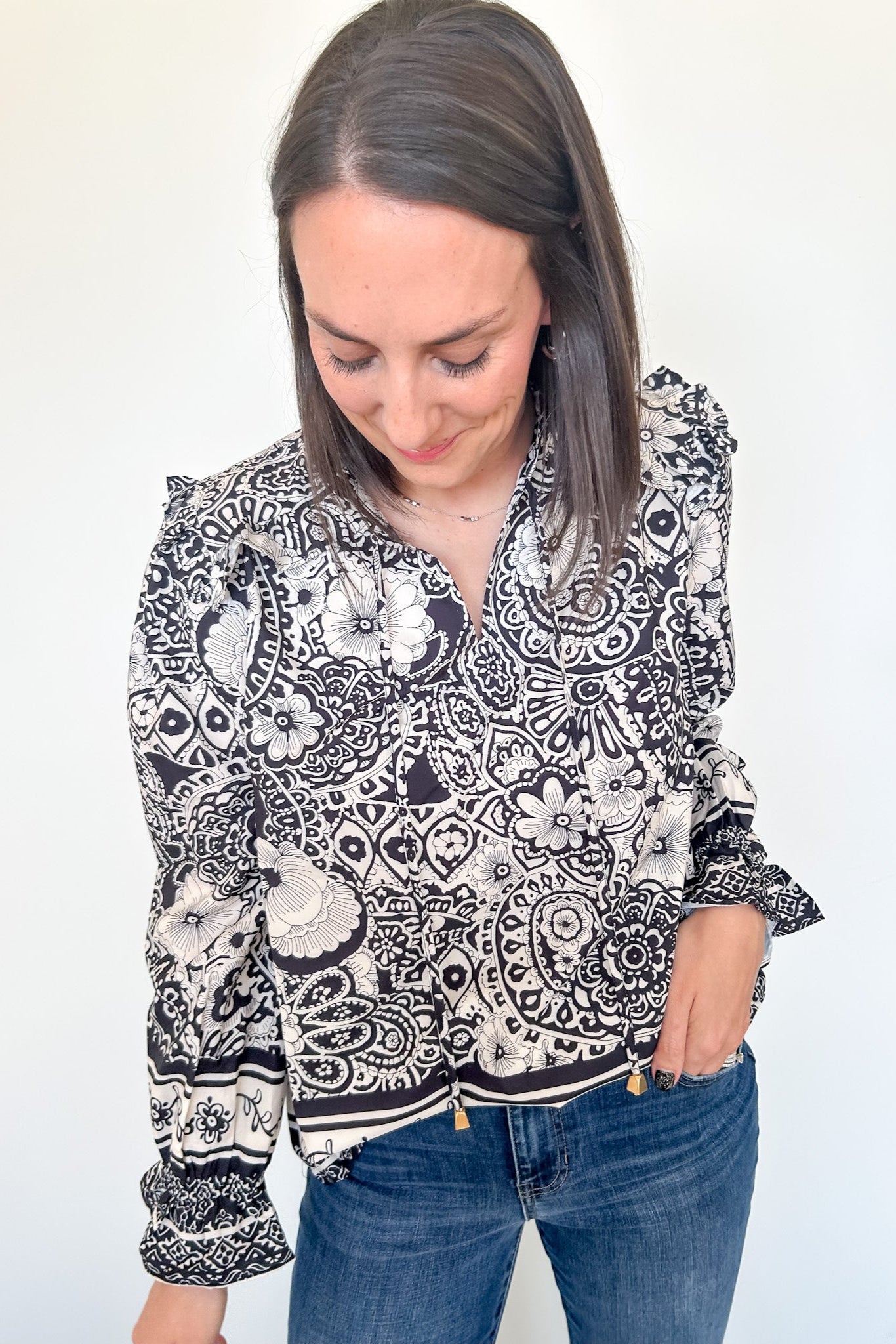 Woman wearing a black and white patterned blouse with blue jeans on a white background