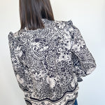 Person wearing a black and white patterned blouse against a plain background