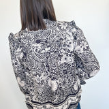 Person wearing a black and white patterned blouse against a plain background