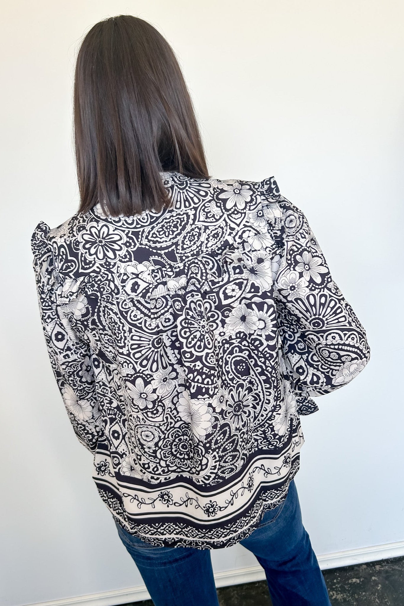 Person wearing a black and white patterned blouse against a plain background
