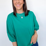 Woman wearing a green top and blue jeans against a white background
