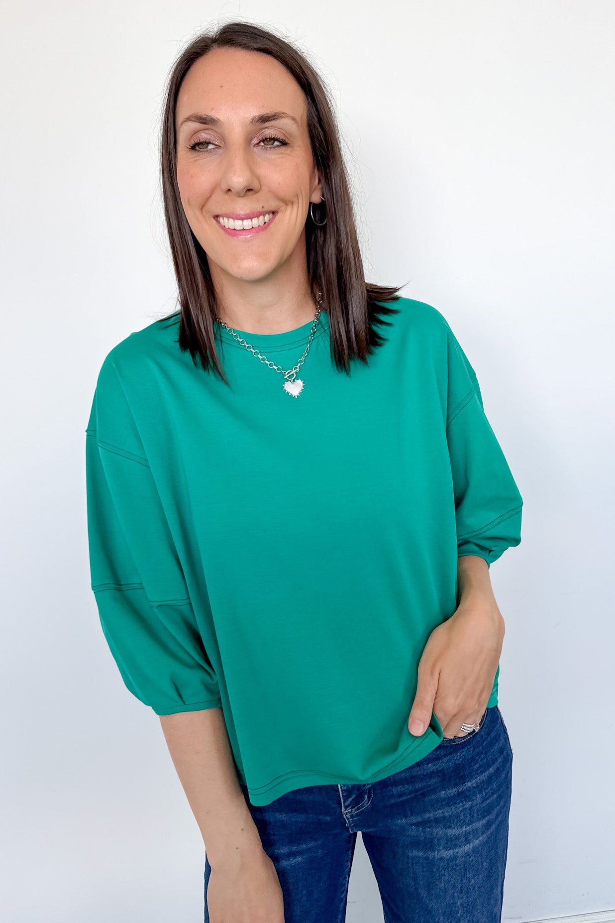 Woman wearing a green top and blue jeans against a white background