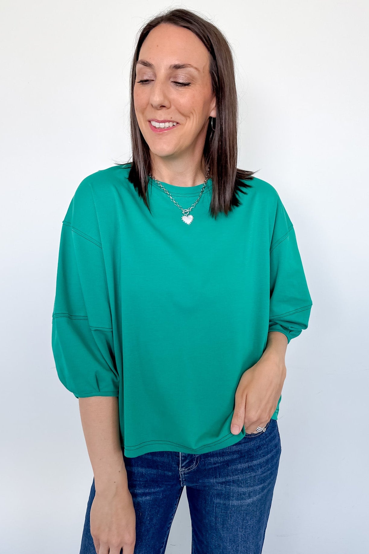 Woman wearing a green top and blue jeans against a white background