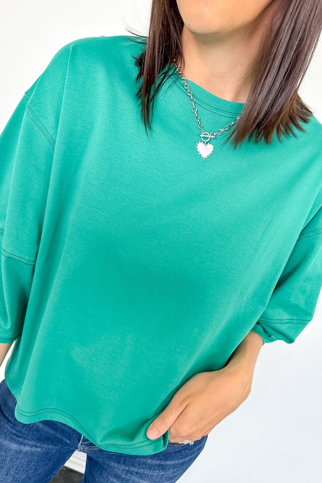 Person wearing a teal oversized t-shirt and blue jeans on a white background