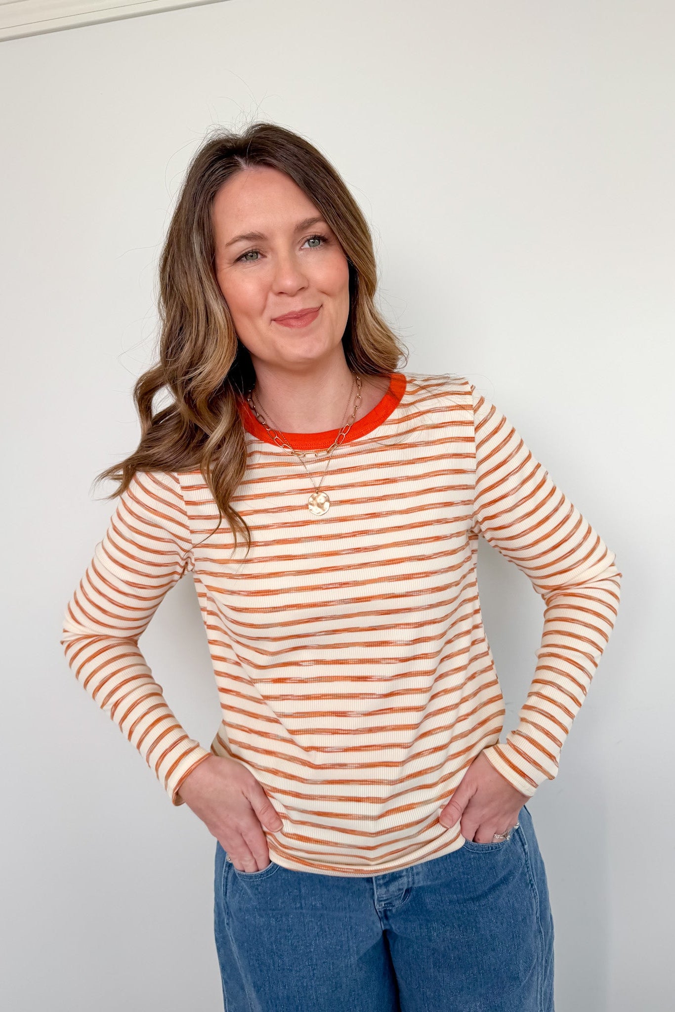 Woman wearing a striped long-sleeve shirt with orange and white stripes against a plain background
