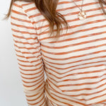 Person wearing a striped long-sleeve shirt with orange and white stripes on a plain background