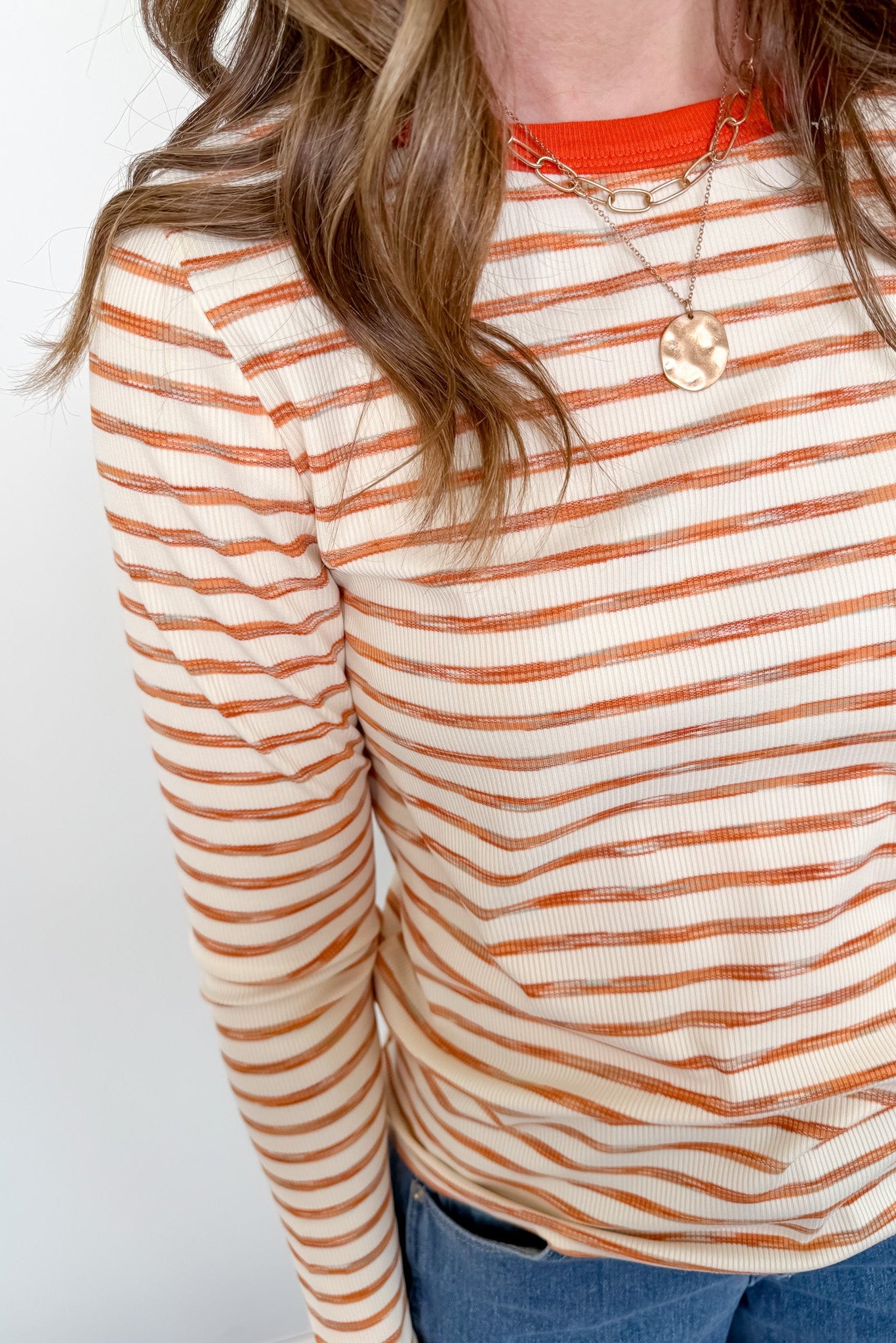 Person wearing a striped long-sleeve shirt with orange and white stripes on a plain background
