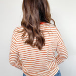 Person wearing a striped shirt and blue jeans against a white wall