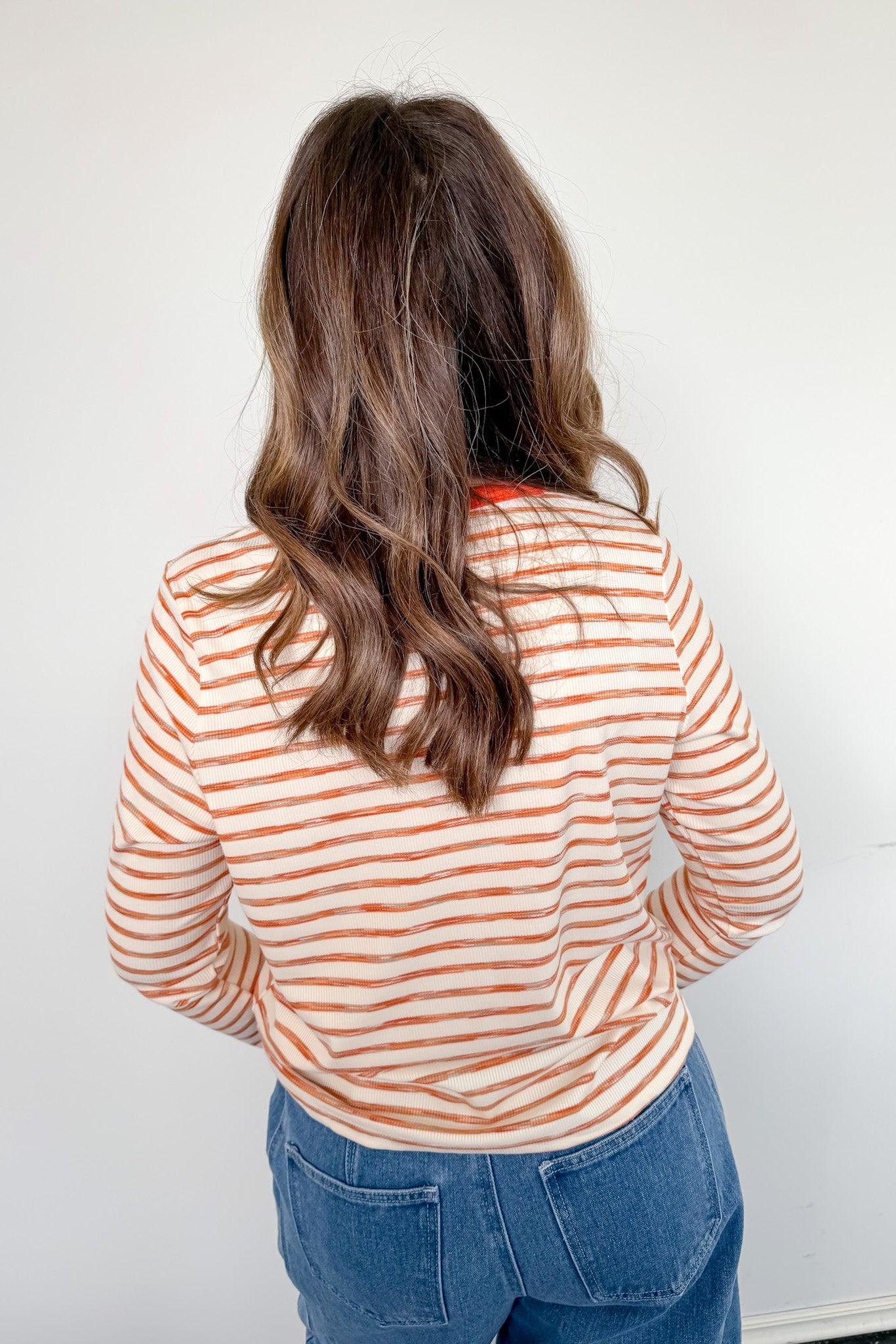Person wearing a striped shirt and blue jeans against a white wall