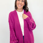 Woman wearing a pink cardigan with pearl embellishments on a white background