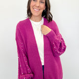 Woman wearing a pink cardigan with pearl embellishments on a white background
