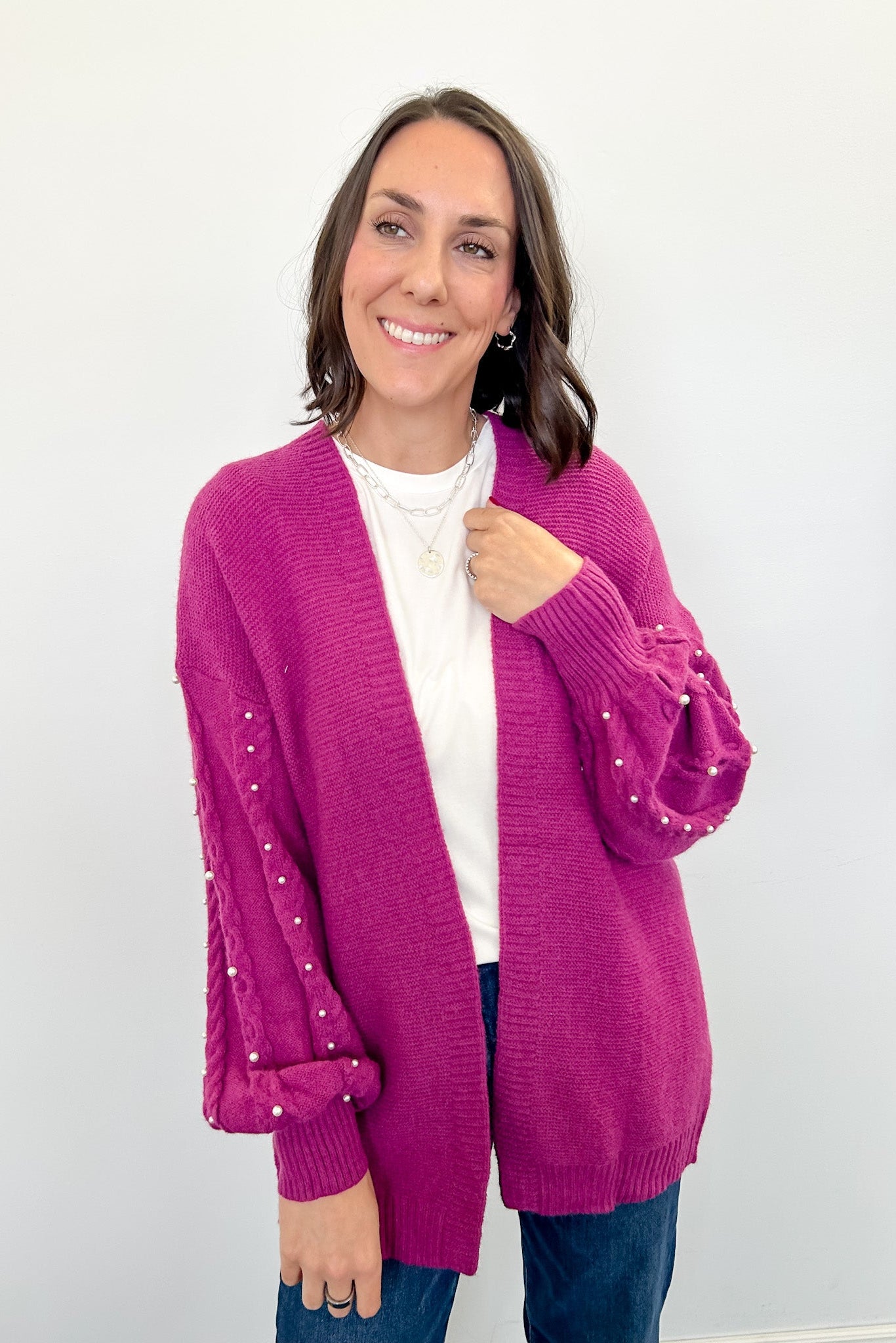 Woman wearing a pink cardigan with pearl embellishments on a white background