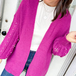 Woman wearing a bright pink cardigan with sequin details, standing indoors.
