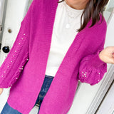 Woman wearing a bright pink cardigan with sequin details, standing indoors.