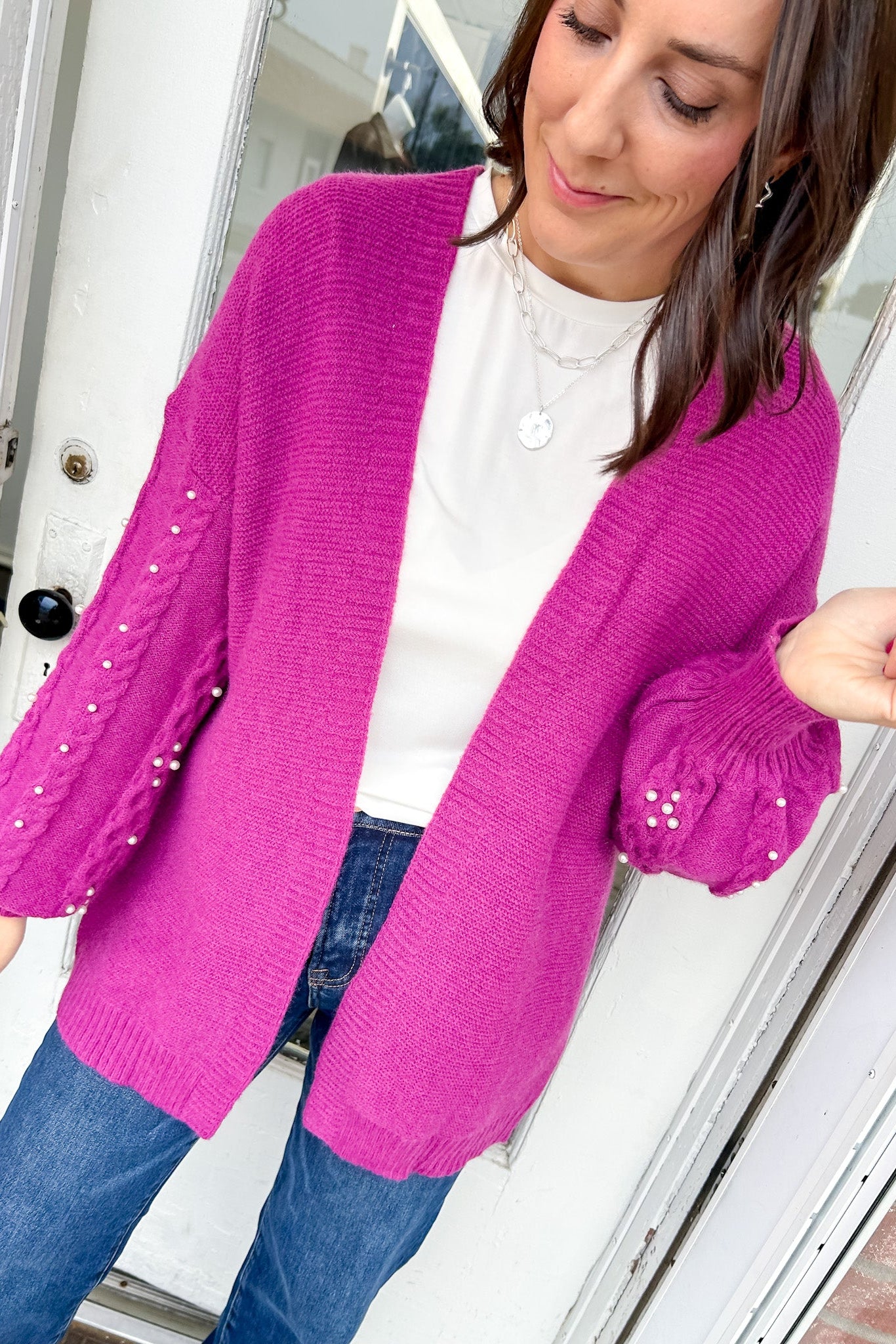Woman wearing a bright pink cardigan with sequin details, standing indoors.