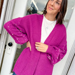 Woman wearing a bright pink cardigan with sequin sleeves indoors.