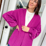 Woman wearing a bright pink cardigan with sequin sleeves indoors.