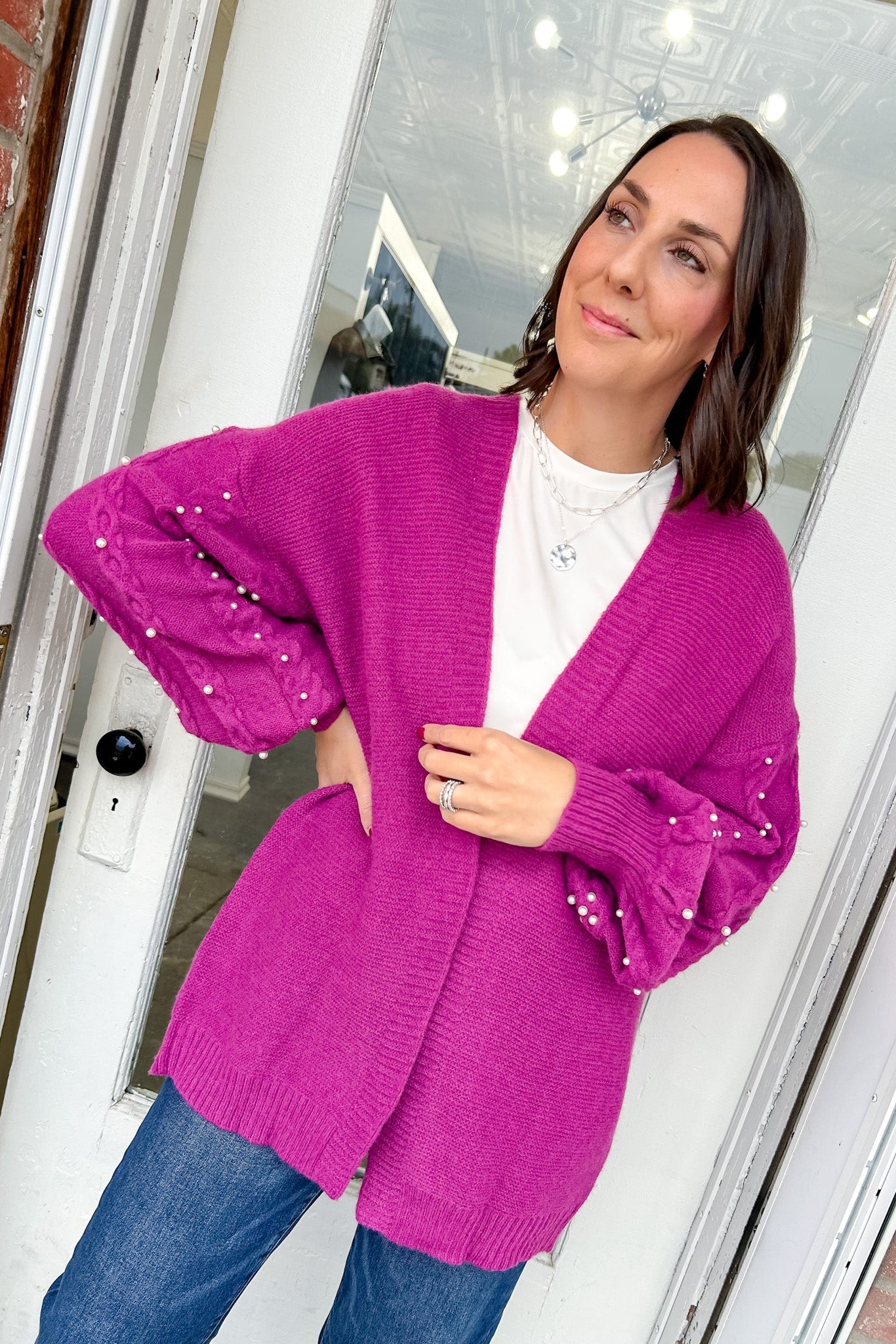 Woman wearing a bright pink cardigan with sequin sleeves indoors.