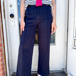 Person wearing a striped shirt with a pink bow, navy pants, and white sandals standing in front of a door.