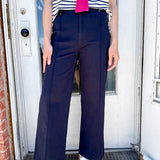 Person wearing a striped shirt with a pink bow, navy pants, and white sandals standing in front of a door.