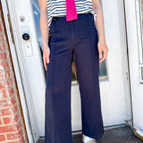 Person wearing a striped shirt, pink scarf, and navy pants standing in front of a door.