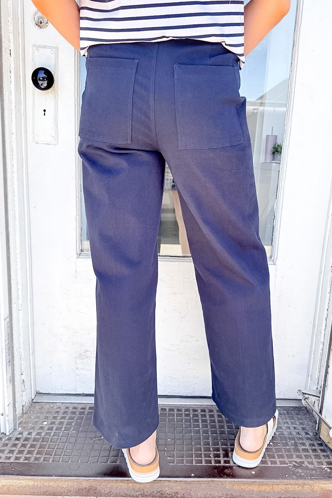 Person wearing navy pants and a striped shirt standing in front of a door.