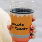 Orange cup with 'made to teach' text held by a person against a white background