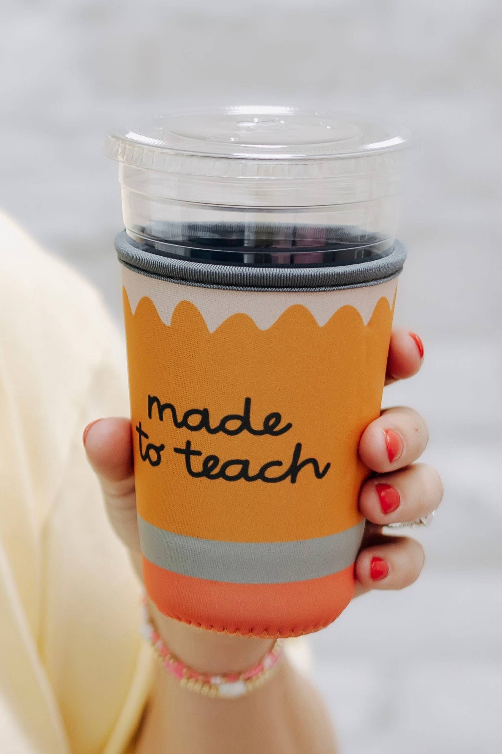 Orange cup with 'made to teach' text held by a person against a white background