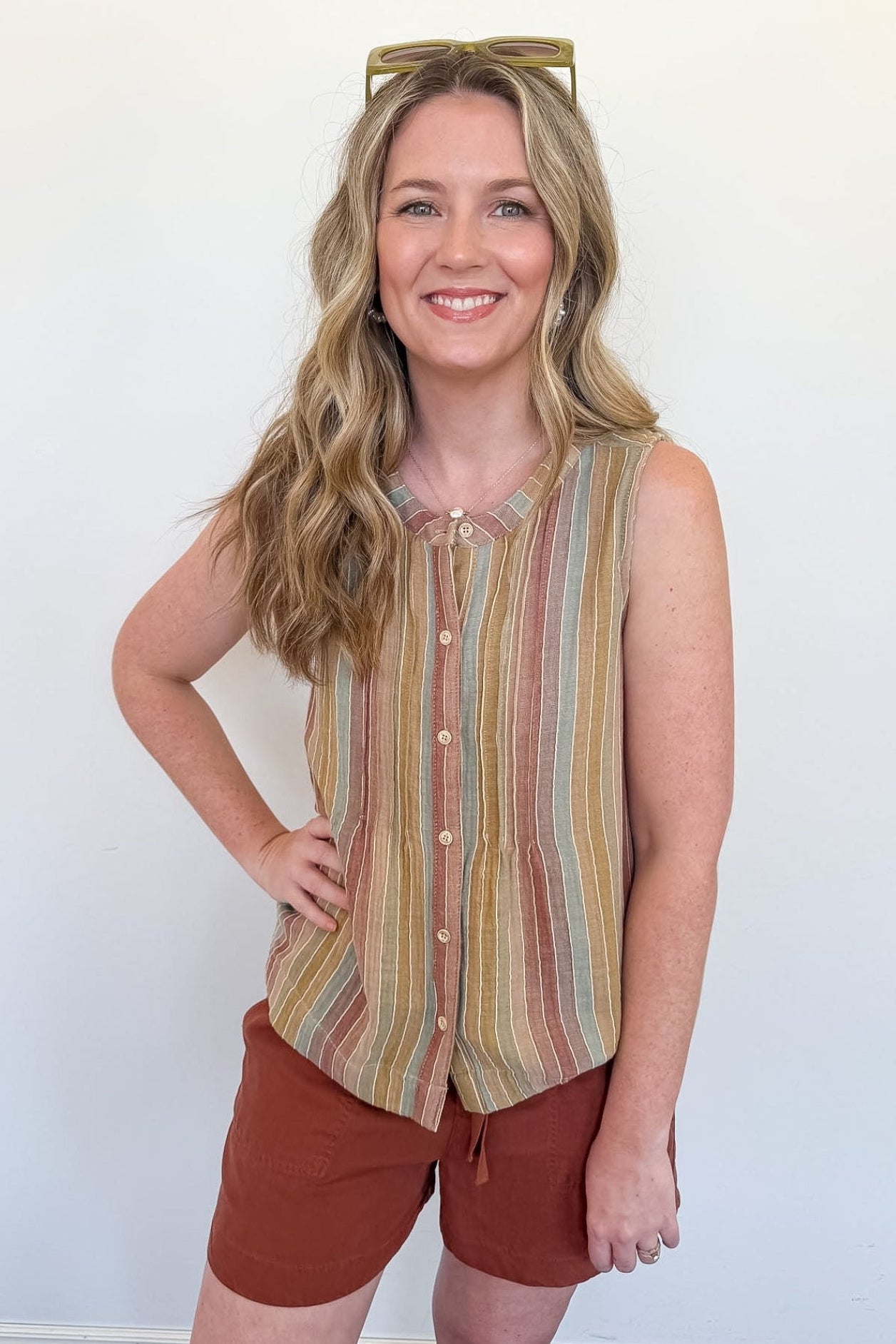 Woman wearing a striped sleeveless top and brown shorts against a white wall