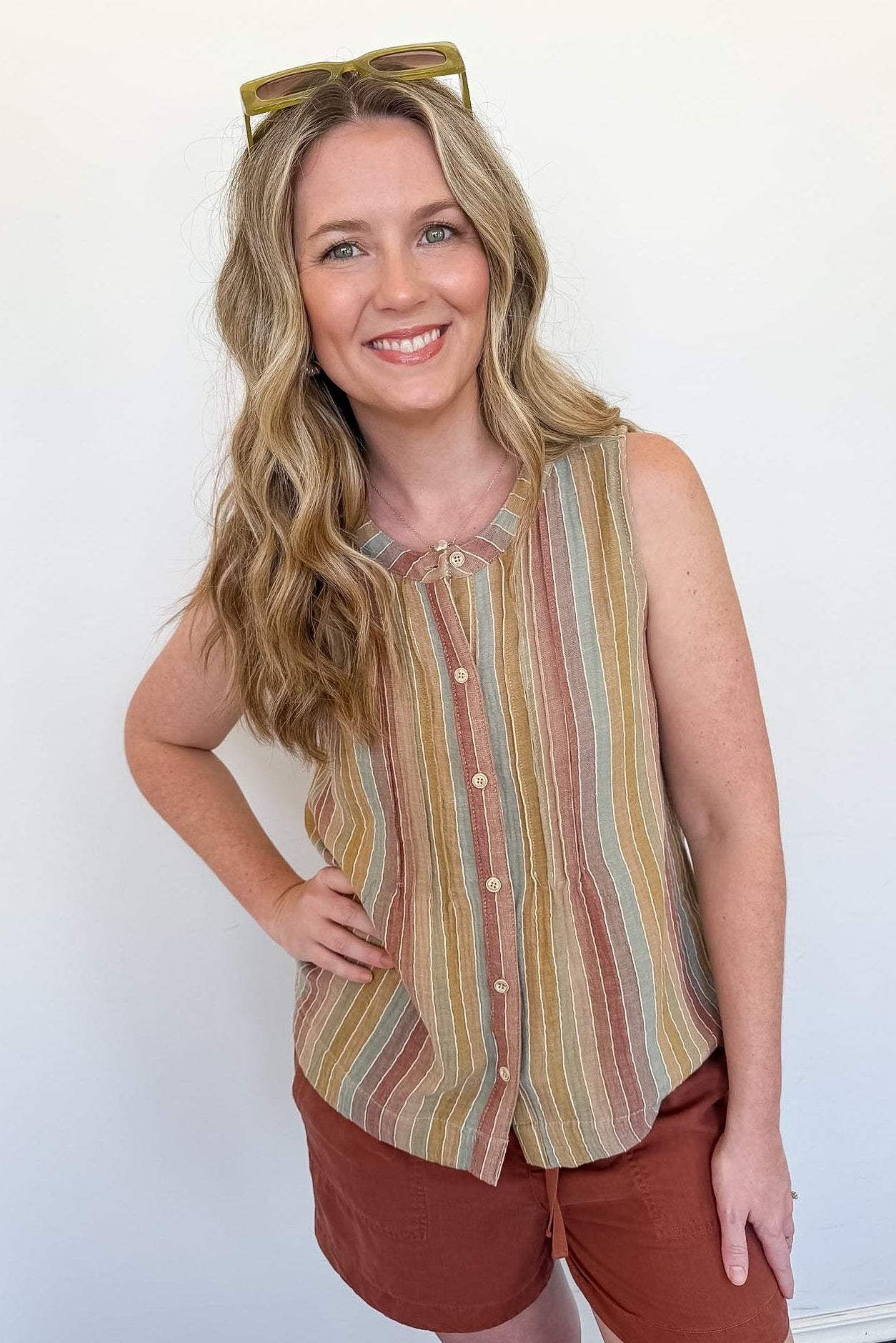 Woman wearing a striped sleeveless top and shorts against a white wall