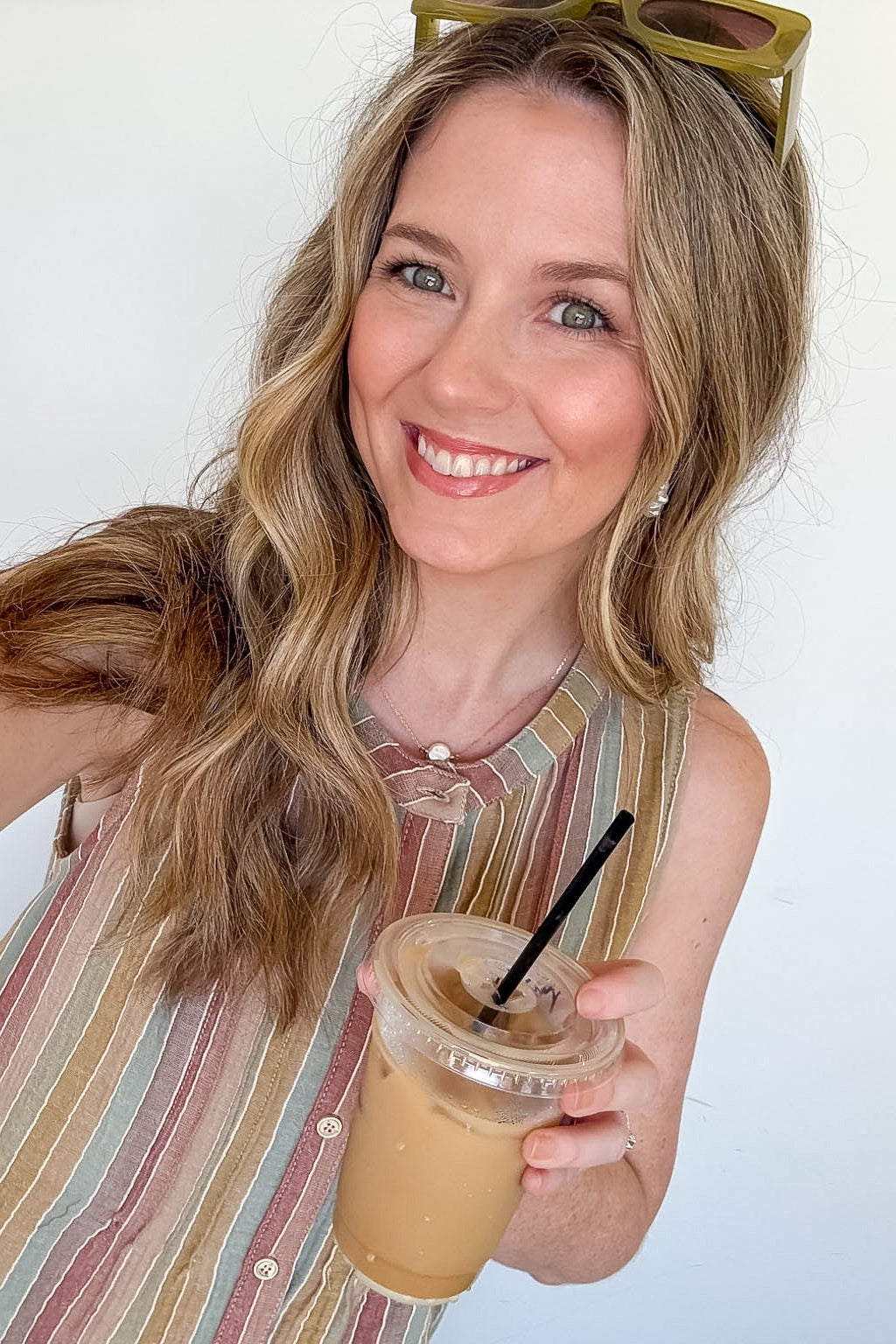 Woman holding a iced coffee drink with a straw against a white background
