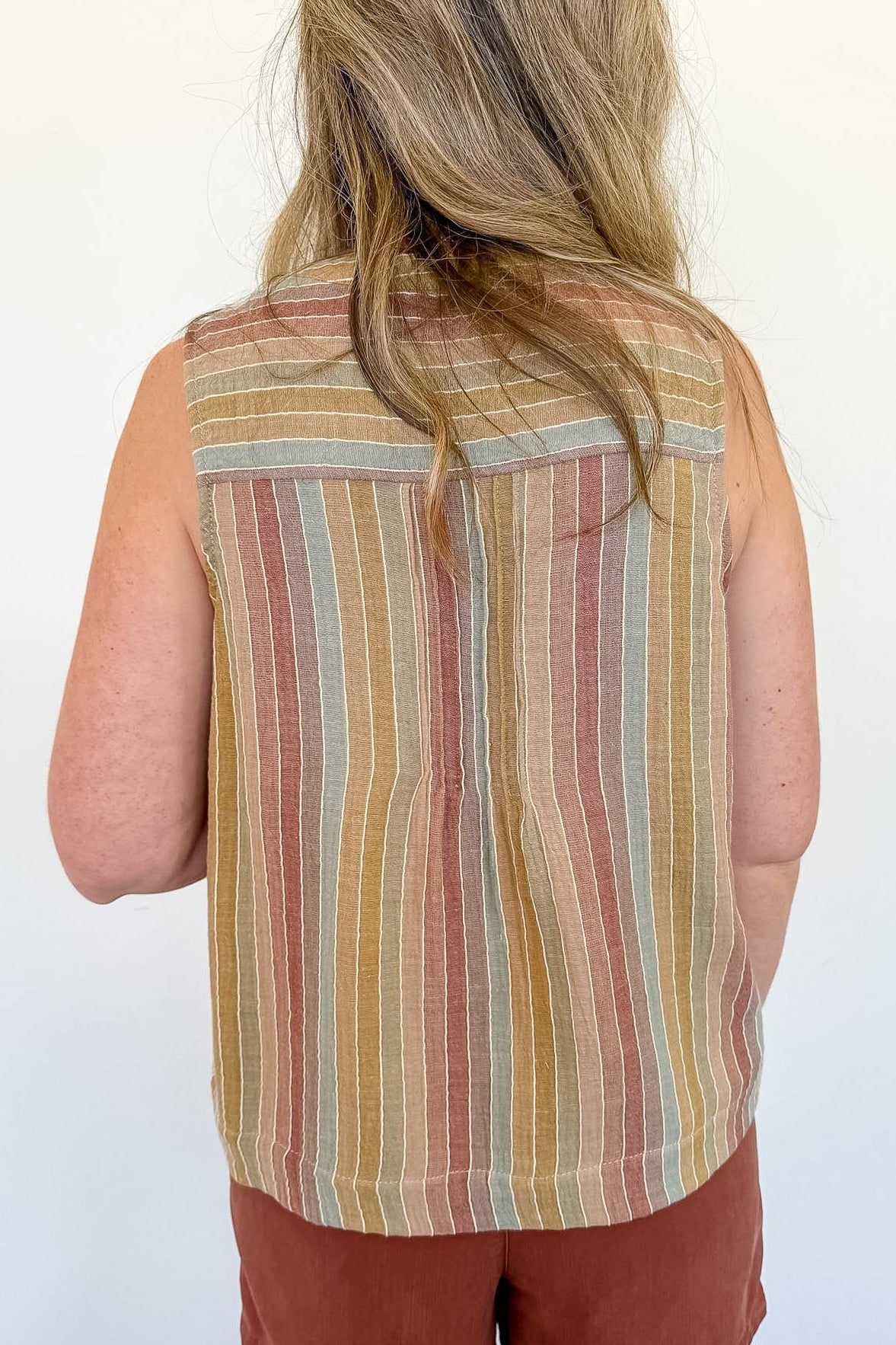 Person wearing a sleeveless striped shirt and red shorts against a white wall.