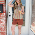 Woman standing in front of a door holding a coffee cup, wearing a striped shirt and shorts.