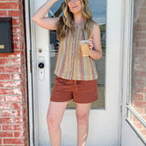 Woman standing in front of a door holding a coffee cup, wearing a striped shirt and shorts.