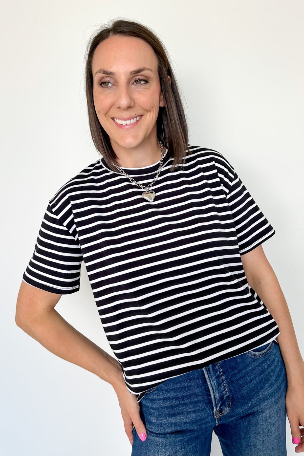 Woman wearing a black and white striped shirt and blue jeans against a white background