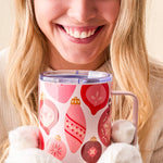 Woman holding a mug with Christmas ornament design, wearing a white sweater and holding a white fluffy blanket.