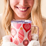 Woman holding a mug with Christmas ornament design, wearing a white sweater and holding a white fluffy blanket.