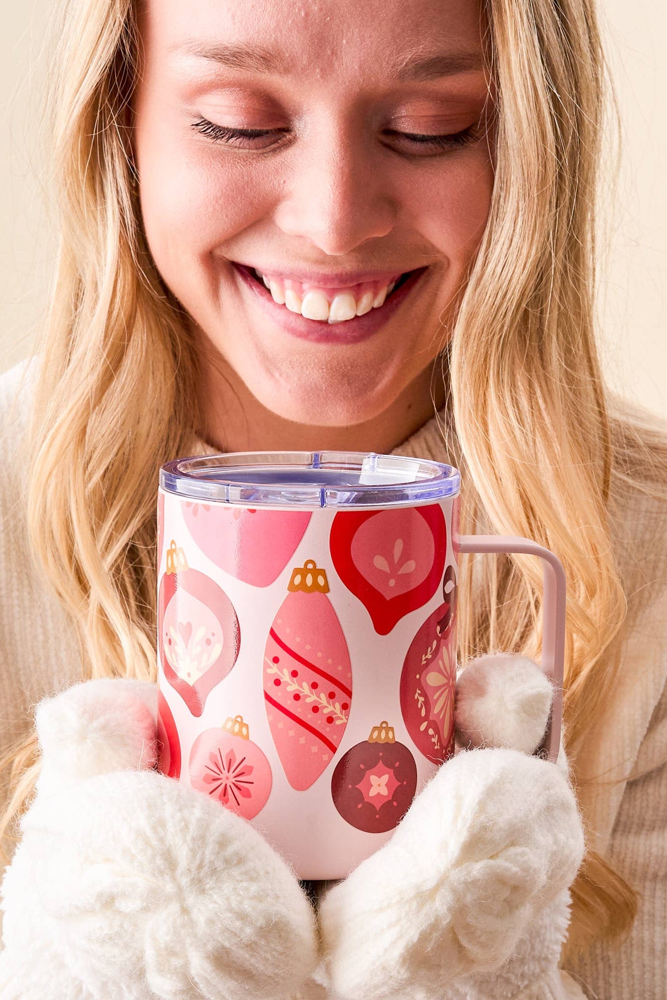 Woman holding a mug with Christmas ornament design, wearing a white sweater and holding a white fluffy blanket.