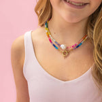 Young girl wearing a colorful beaded necklace against a pink background