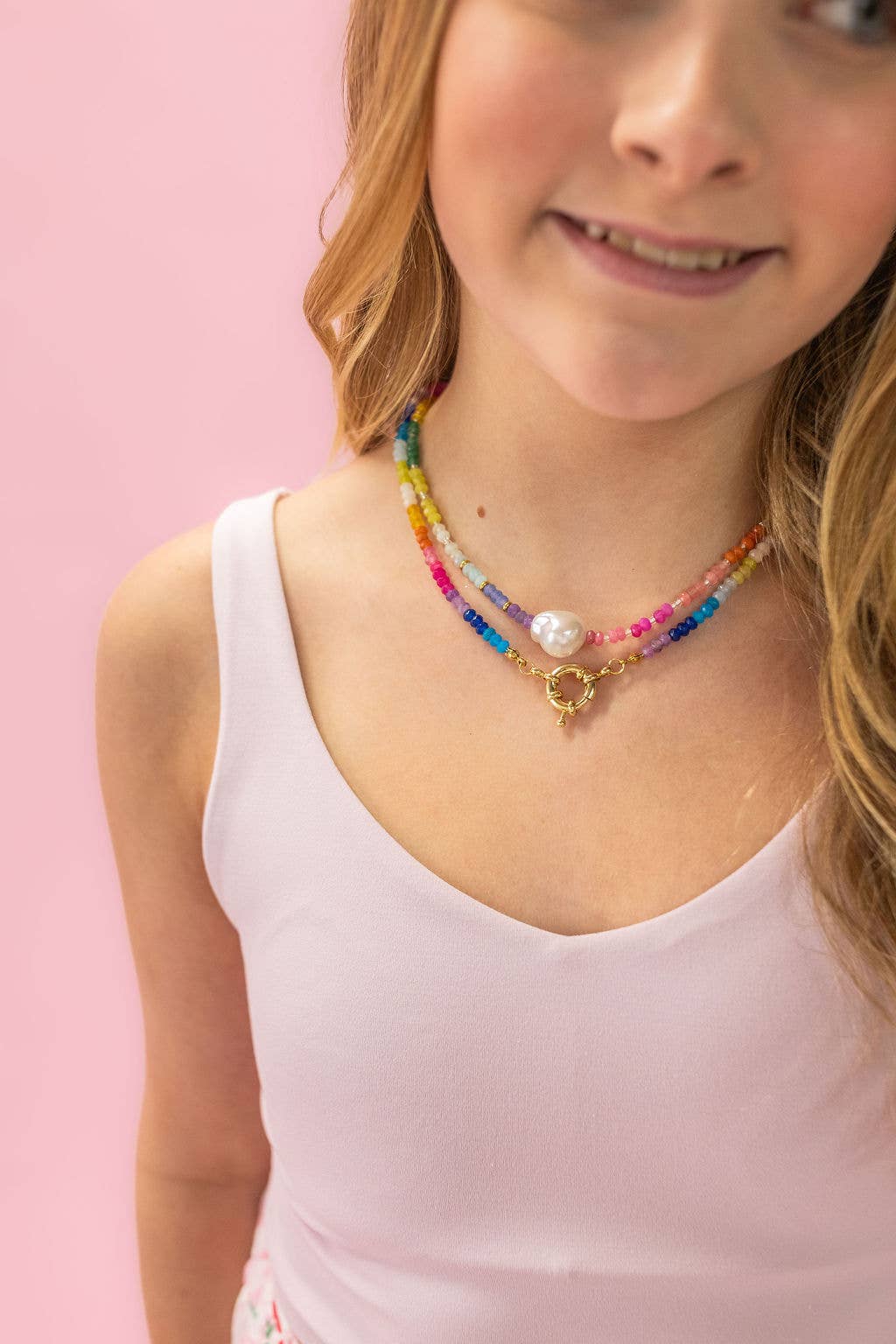 Young girl wearing a colorful beaded necklace against a pink background