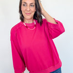 Woman wearing a bright pink sweatshirt and blue jeans against a white background