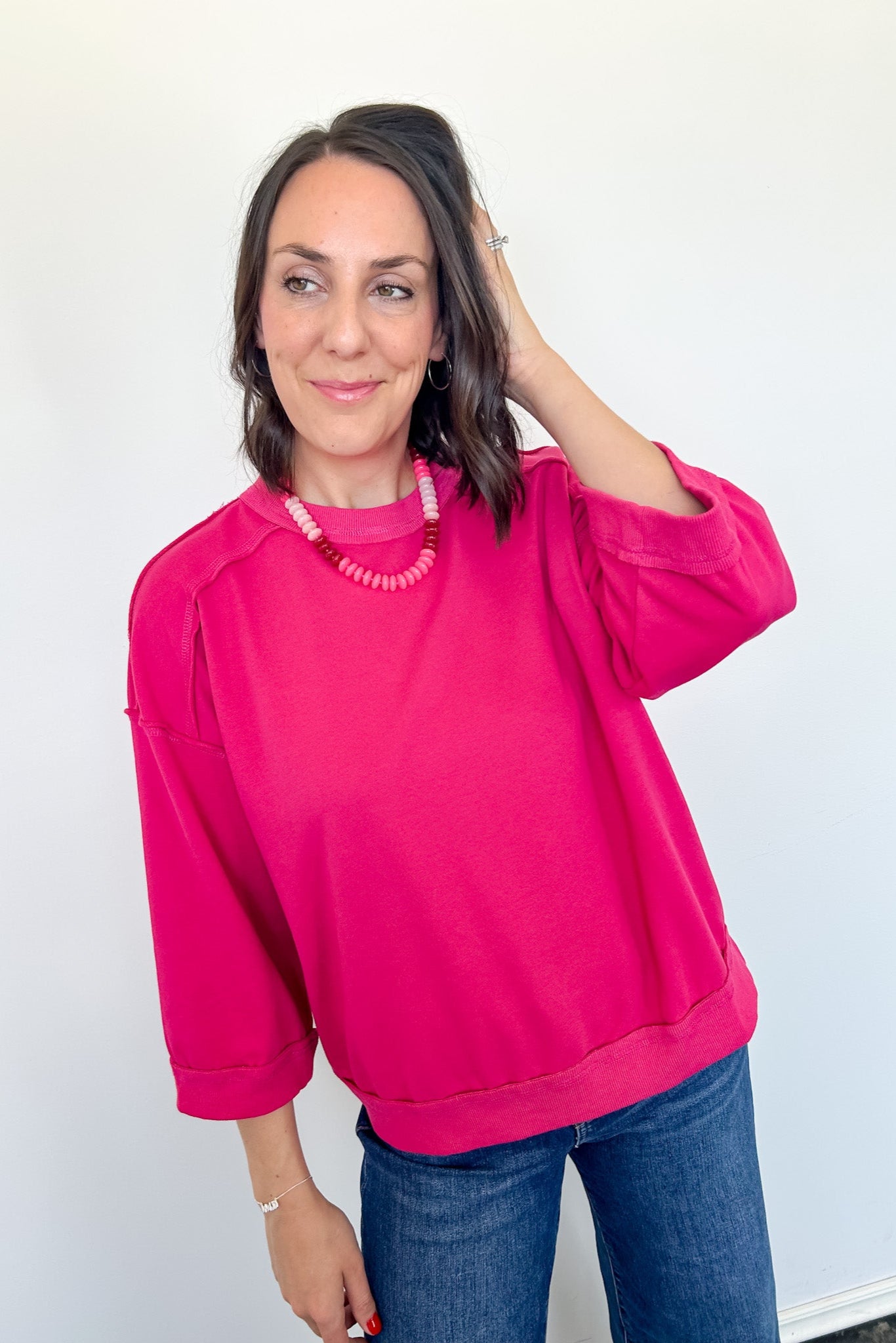 Woman wearing a bright pink sweatshirt and blue jeans against a white background